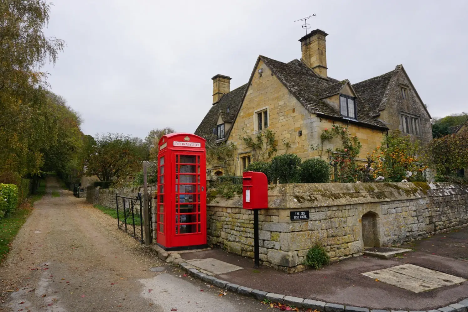 Bright red telephone box and post box contrast against the honey-coloured Cotswold cottage in Stanton
