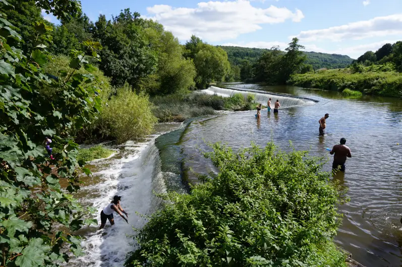 People swimming in the River Avon and playing near the cascades of Warleigh Weir